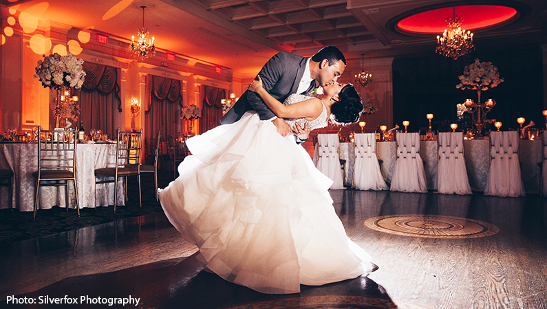 Bride and groom dancing in ballroom with orange uplighting